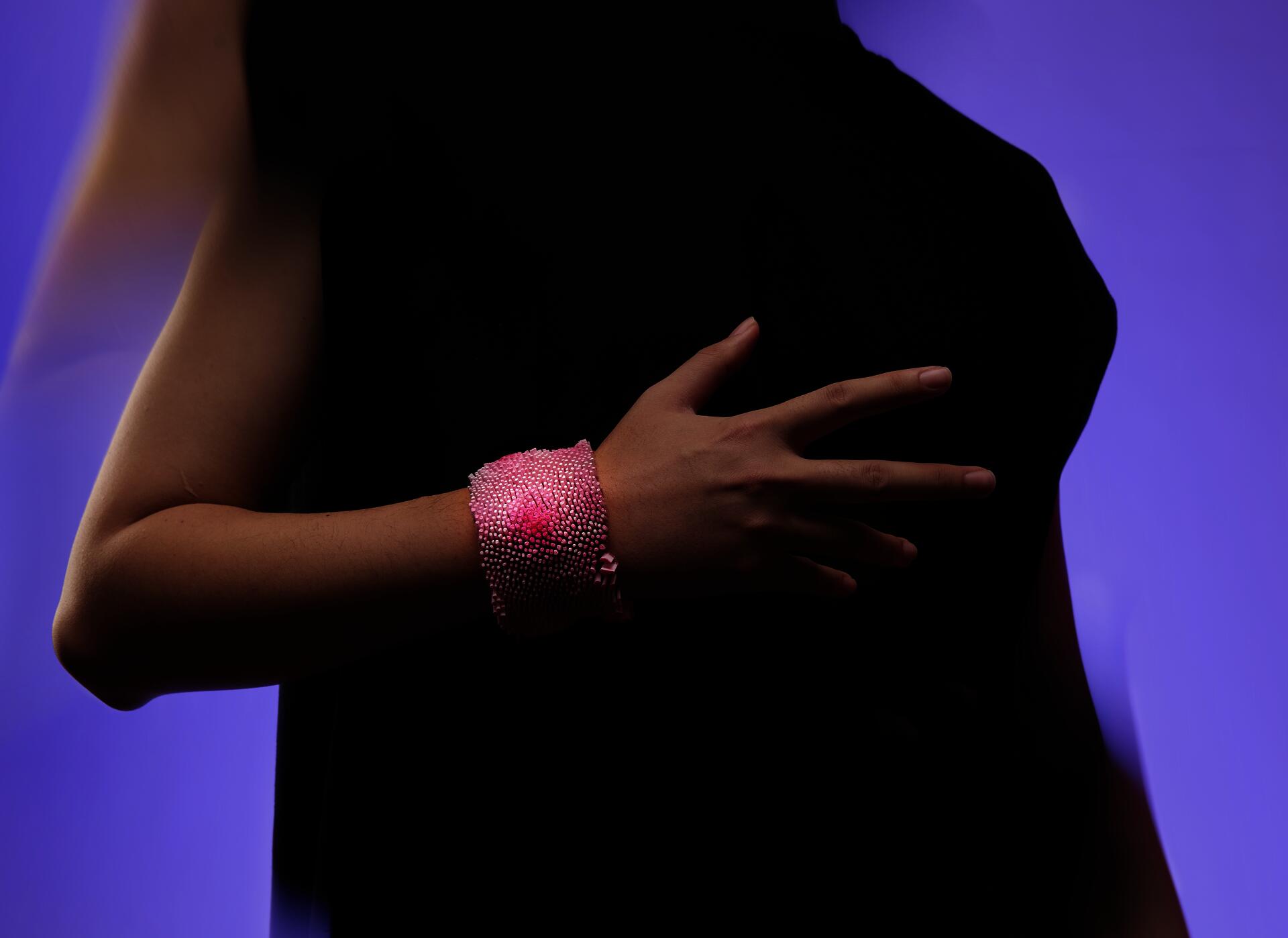 Pink bracelet covered in densely packed small upright elements on mesh, with darker pink areas creating depth variation.