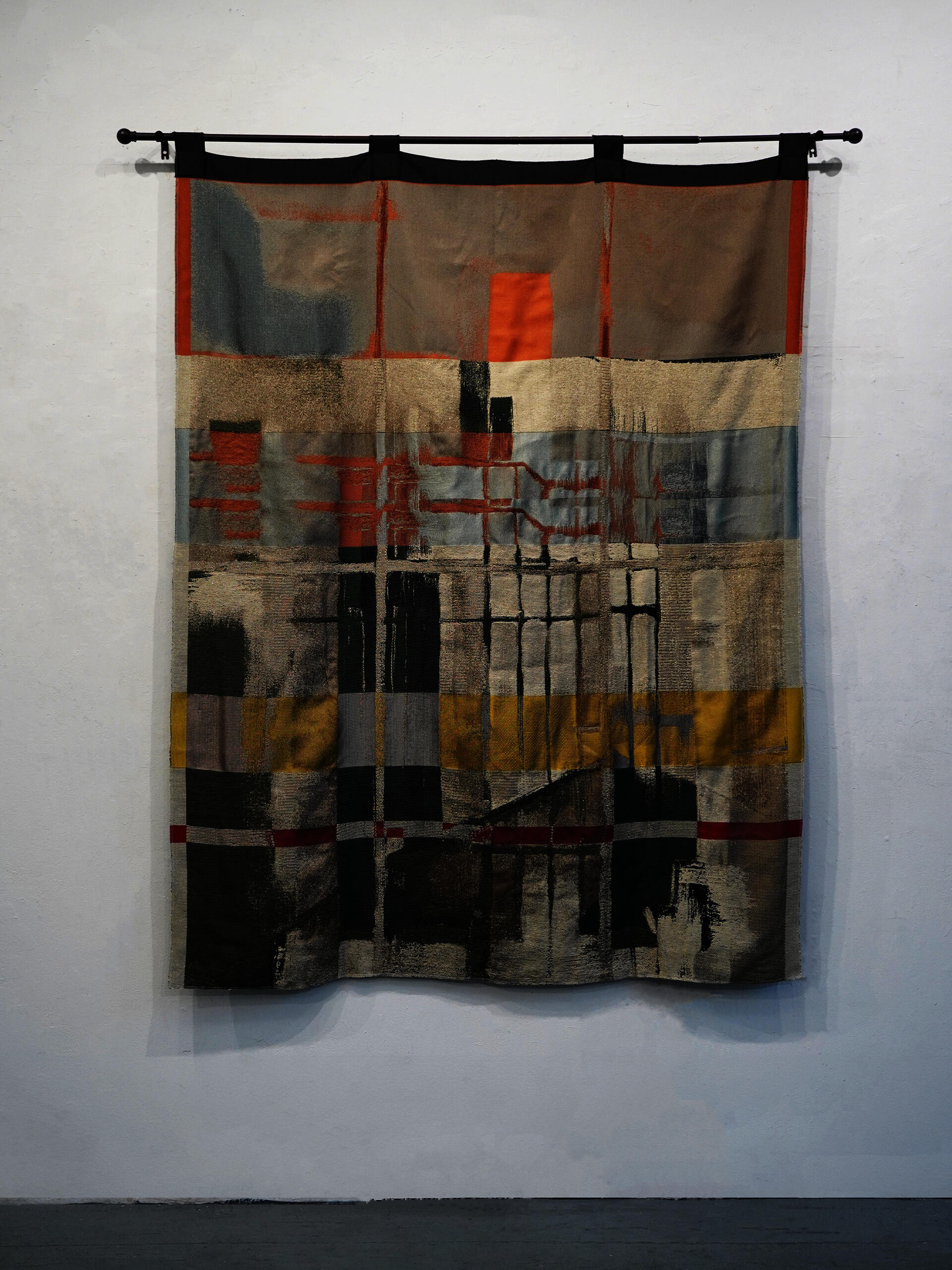 A woven curtain reproducing a painting of a courtyard viewed from within. The composition is divided by a window grid opposite, its panes structuring fields of warm sunset-lit color