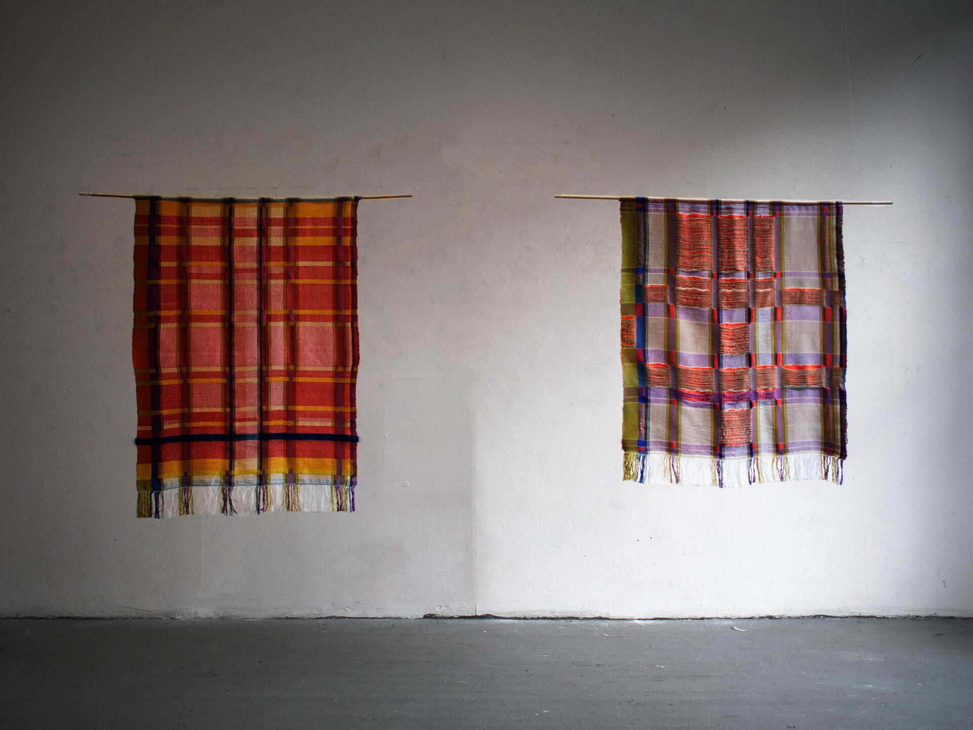 Two handwoven textiles hung side by side, each depicting a pattern derived from an Italian Renaissance building. The pieces mirror one another with an unsettling, near-identical symmetry