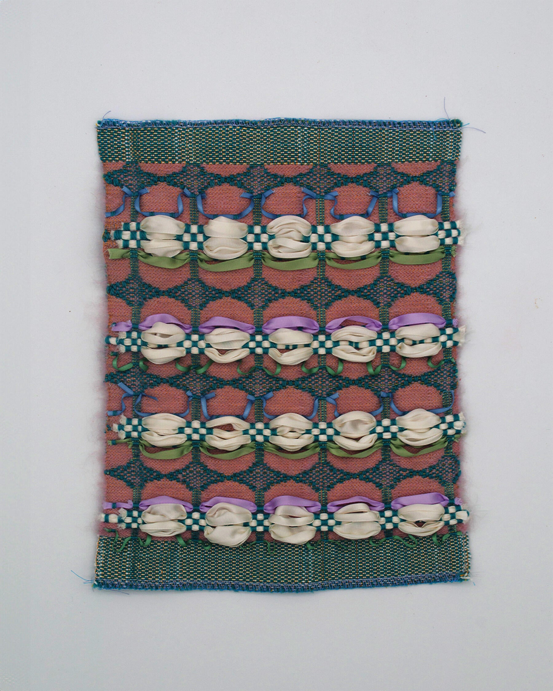 A woven fabric with a teal lace pattern surrounding desaturated pink oblongs. White ribbons form voluminous curves across the surface, resembling piped cream, anchored by a teal checkered weave