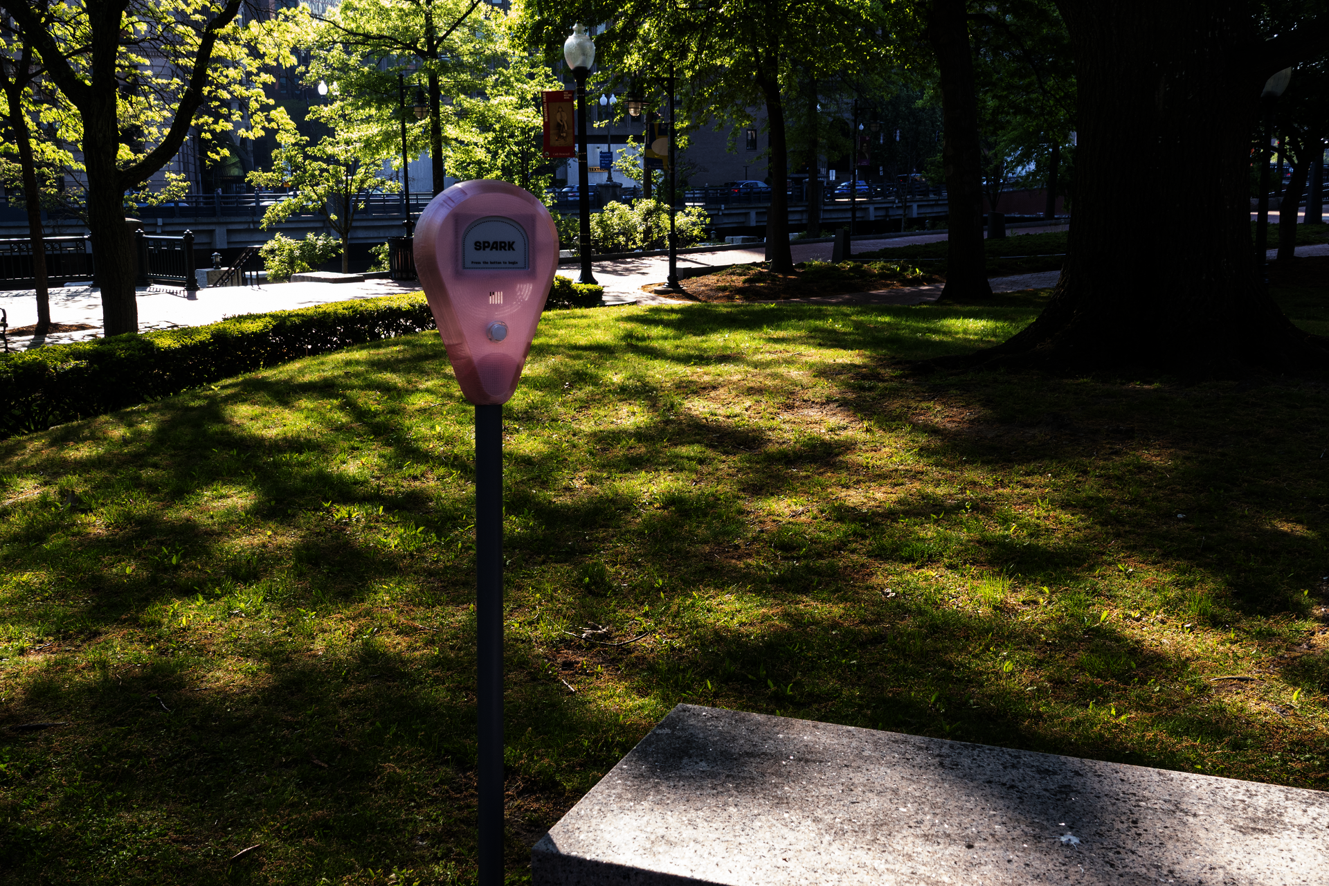 Spark device standing on grass near the river, surrounded by trees, shadows, and city park scenery.