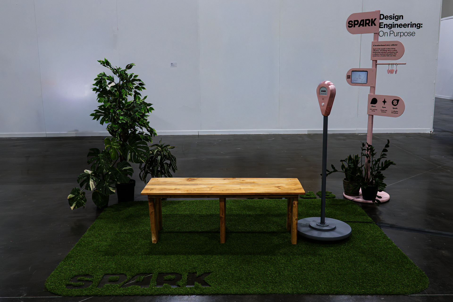 Spark exhibition setup with artificial grass, wooden bench, plants, and signage.