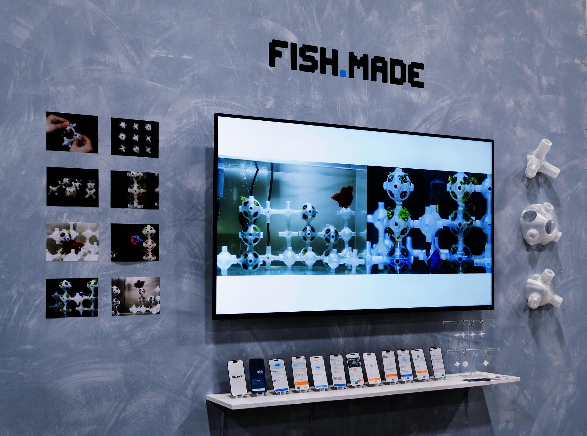 FISH.MADE exhibition setup featuring a screen with generated habitat structures, a fish tank prototype, modular 3D-printed components, and app interface mockups.