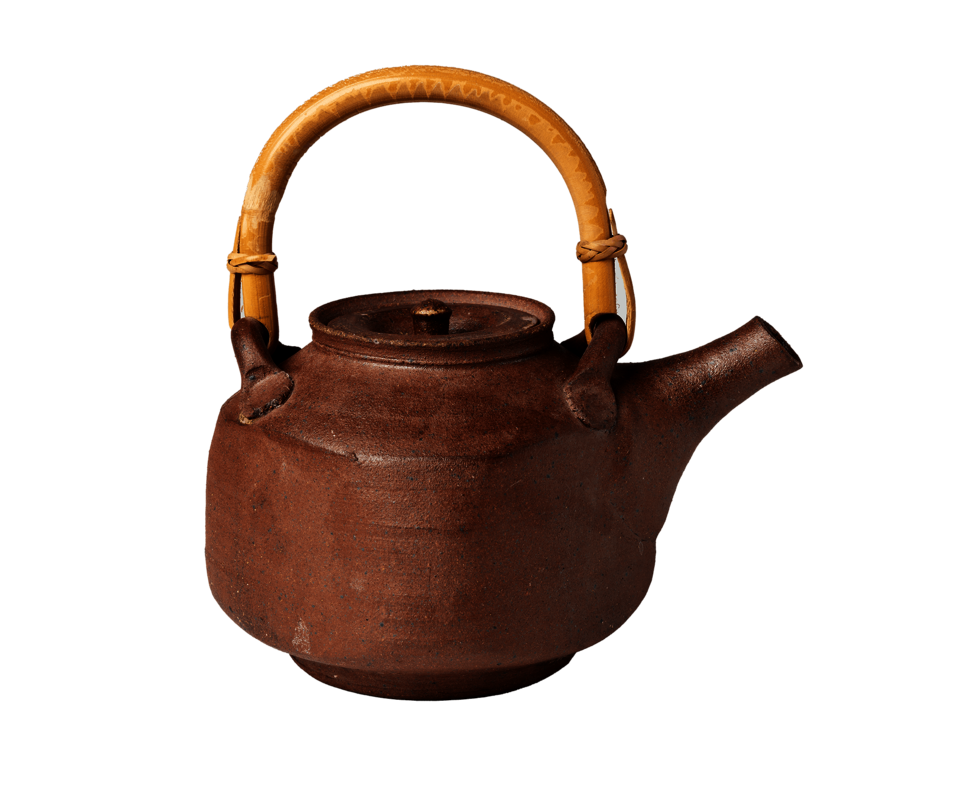 Square-shaped brown teapot resting on circular foot. Rounded tan handle on top of teapot.