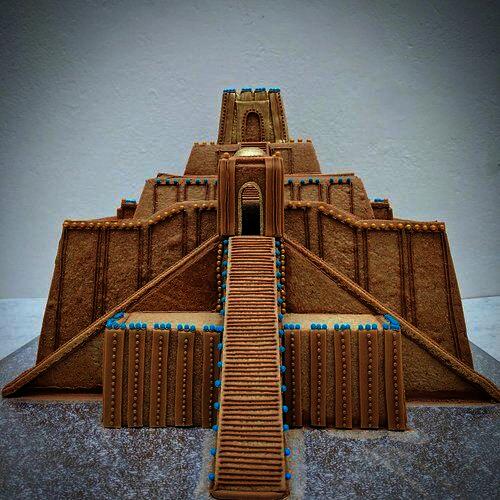 Color photograph of a gingerbread model of the Ziggurat of Ur. Light brown cookie slabs form the stepped layers and large sloping staircases, with little blue green pastilles as decorative elements.