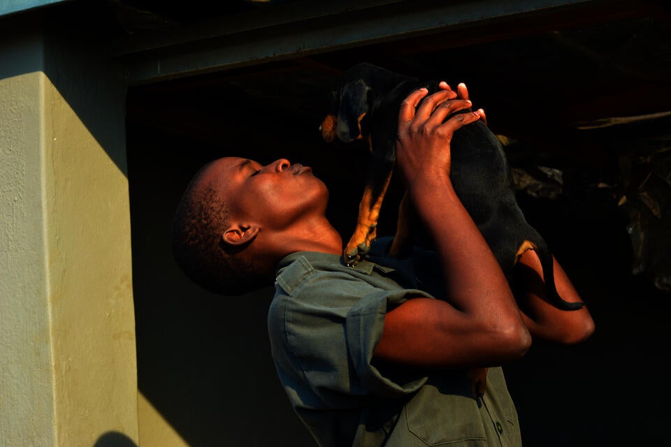 Precious, an anti-poaching dog trainer holds up and kisses a new puppy from their team.