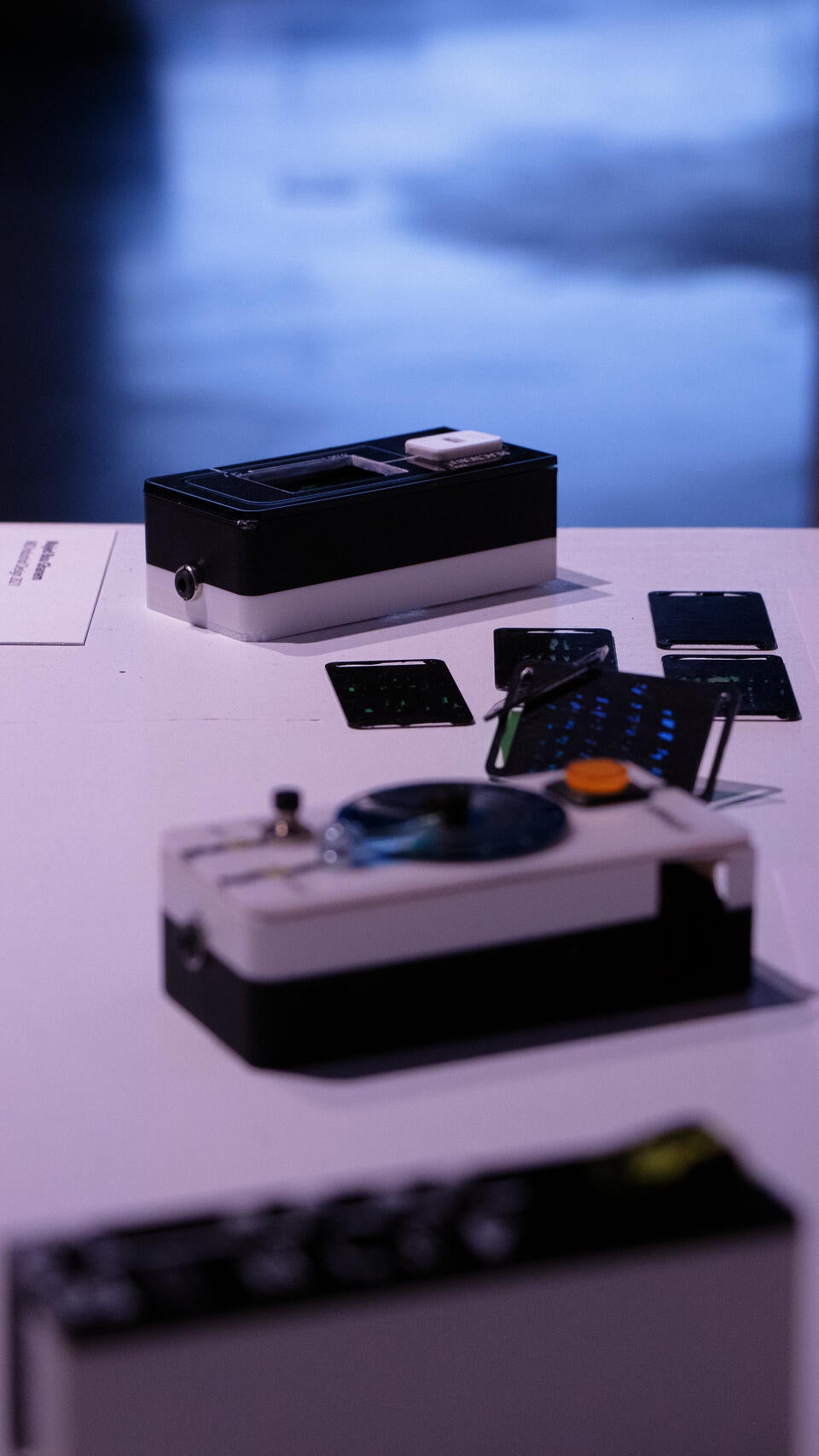 Portrait oriented photograph (vertical) showing the three devices. top to bottom: reaction tile, monofilter, vibelist. The reaction tile is in focus, the rest are blurry.