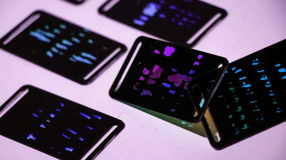 Closeup shot of 5 reaction tiles placed on a surface. the engraved parts are translucent and let light through. the angle of the light changes the transmitted and reflected colors.