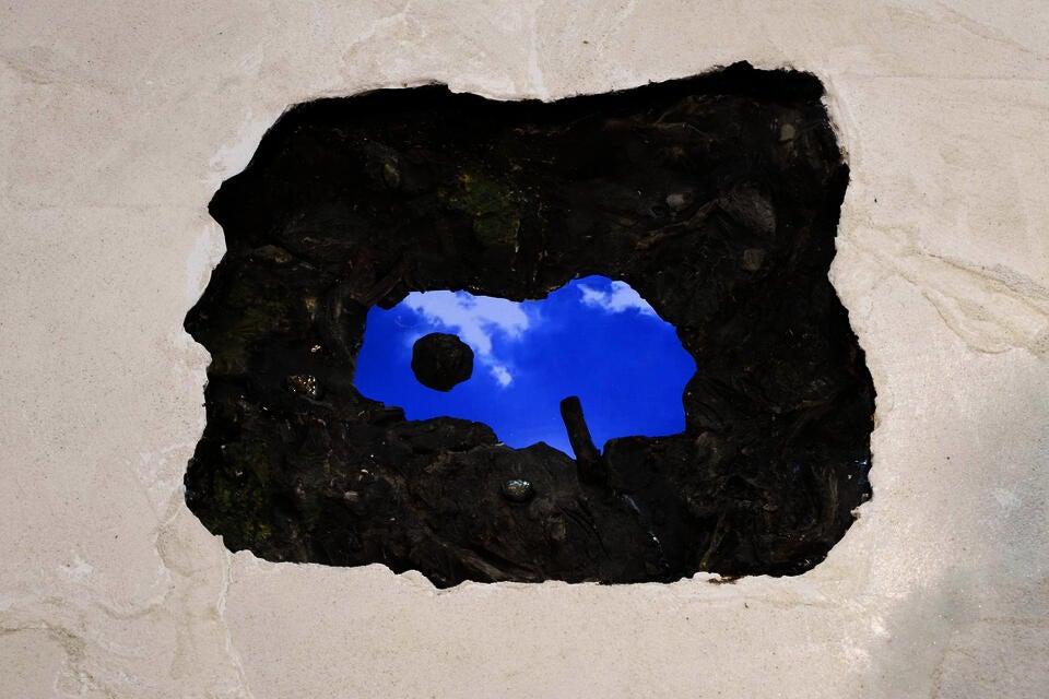 Sculpture of puddle with electronic screen inside playing videos of clouds, cattails  and the artist drawing in sand.