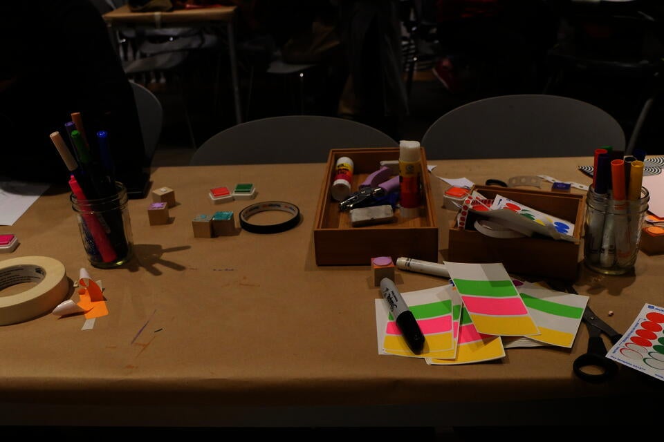color photograph of a table covered in brown paper, topped with piles of various art supplies