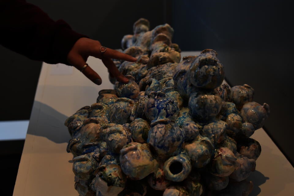 color photograph of a hand with a few rings touching a ceramic sculpture resembling a pile of small orbs