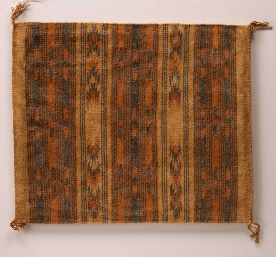 Textile with stripes. Each stripe has a subtle geometric pattern running through it. Palette is peach, tan, and dark blue. Object is square shaped, with small tassels at each corner.