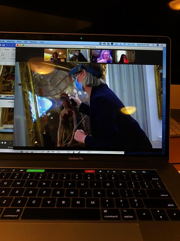 Screenshot of a Zoom session. In the main image, a masked figure interacts with a painting. A gallery of participants watches at the top.