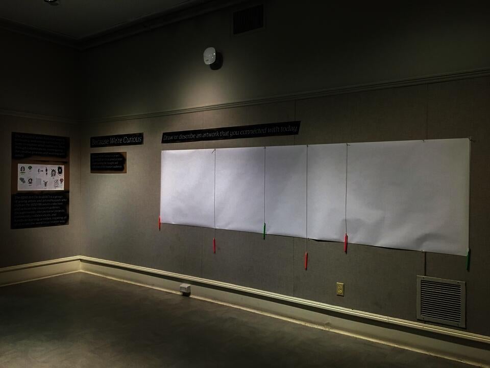 Wall with cardboard signs with laser cut lettering, and a large sheet of blank paper with pens attached.