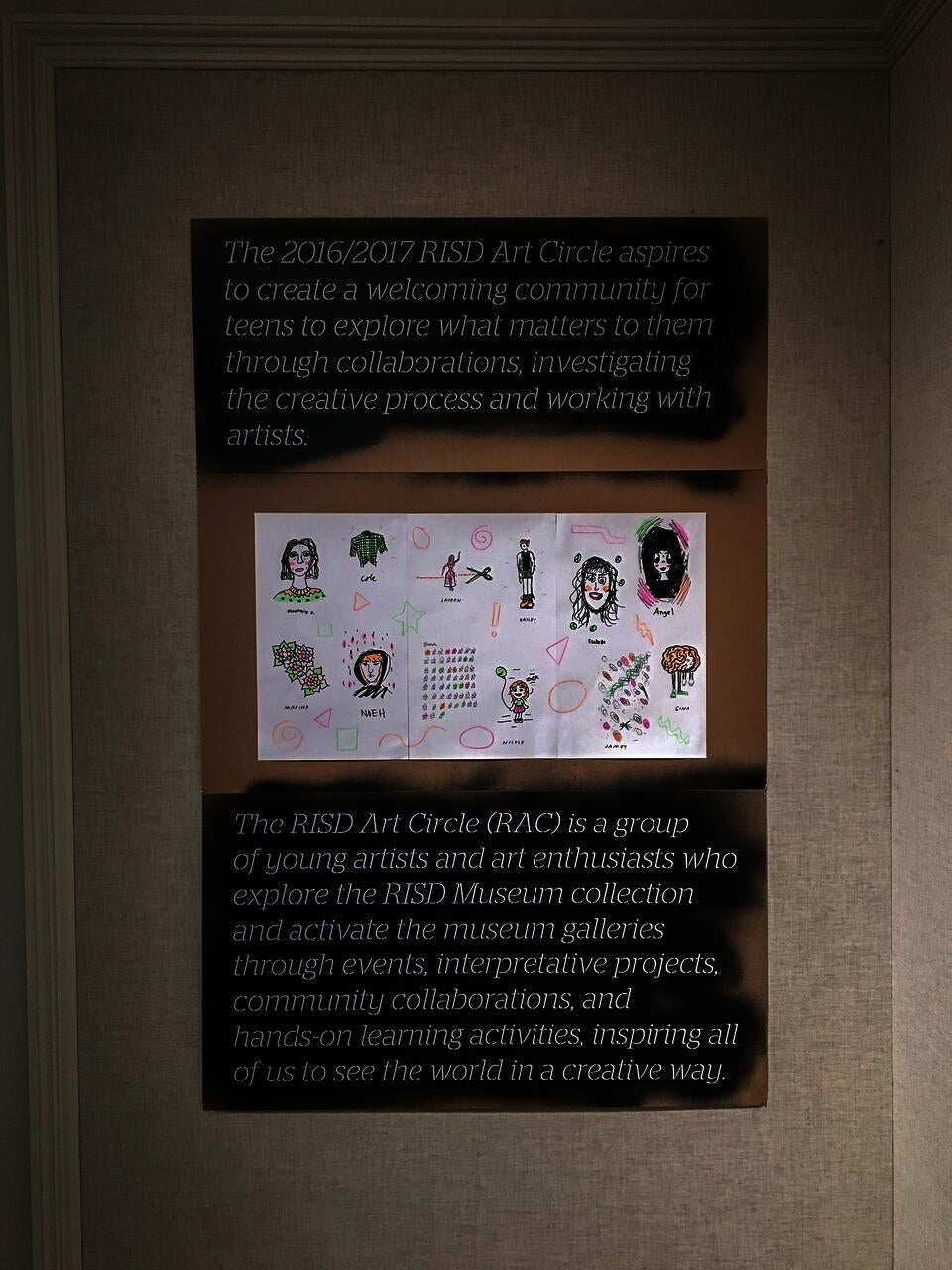 Cardboard panel with laser cut lettering with the RAC 2016/17 mission statement, and a sheet of colorful drawings.