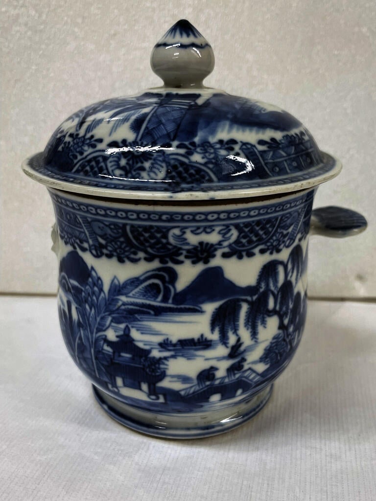 A white ceramic sugar bowl with flat handles and lid, the decorations are architectural and floral. 