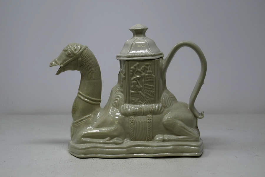 A completely white earthenware camel shaped teapot with a hexagonal lid.