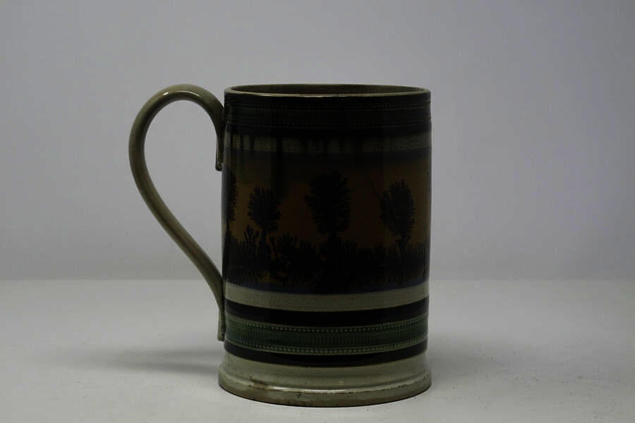 An earthenware tankard that has white, blue, orange, green, and dark brown/black glaze vertical decorations.