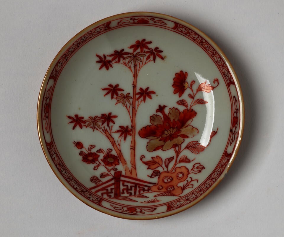 A porcelain teacup with iron-red and gold floral, structural, and abstract decorations. 