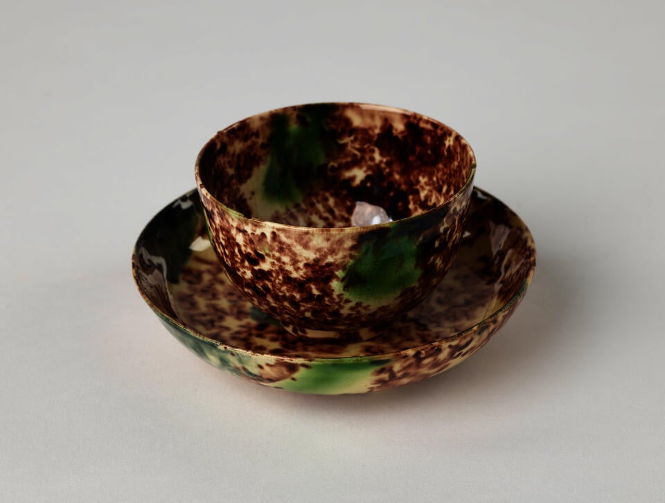 A ceramic cup and saucer that is white, brown, and green in color. 