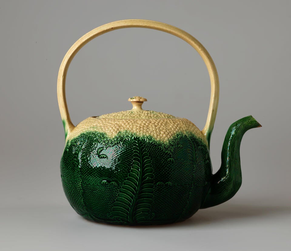 A cream and green punch pot with floral decorations, a tall handle that is directly above the lid.