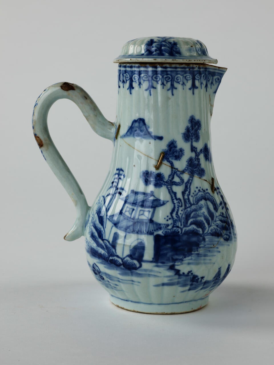 A white chocolate pot with blue decorations depicting floral and architectural elements.