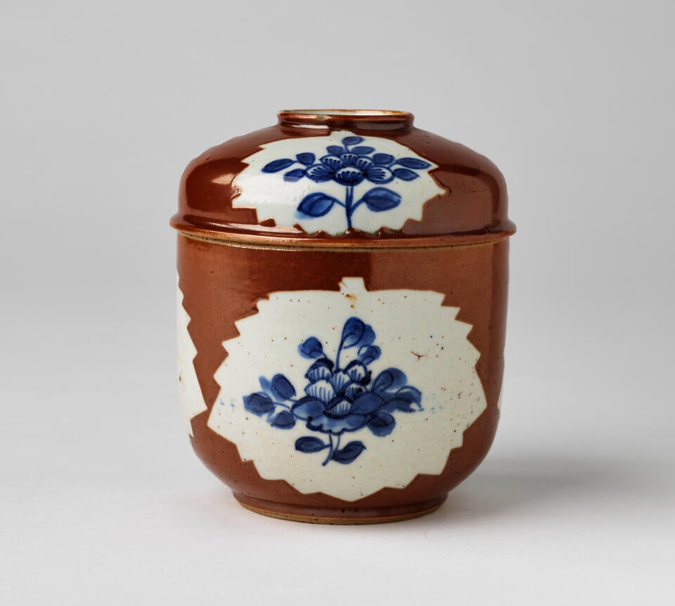 A ceramic covered bowl that is white, brown and has blue floral decorations.