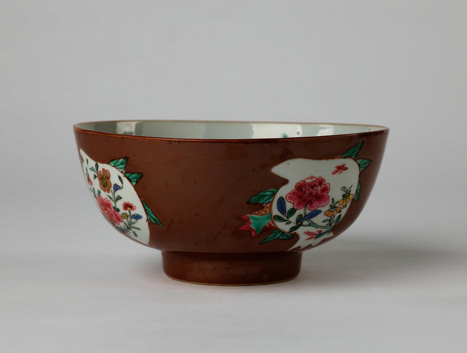 A white and brown ceramic bowl with green, yellow, and pink floral decorations with a short, small foot.