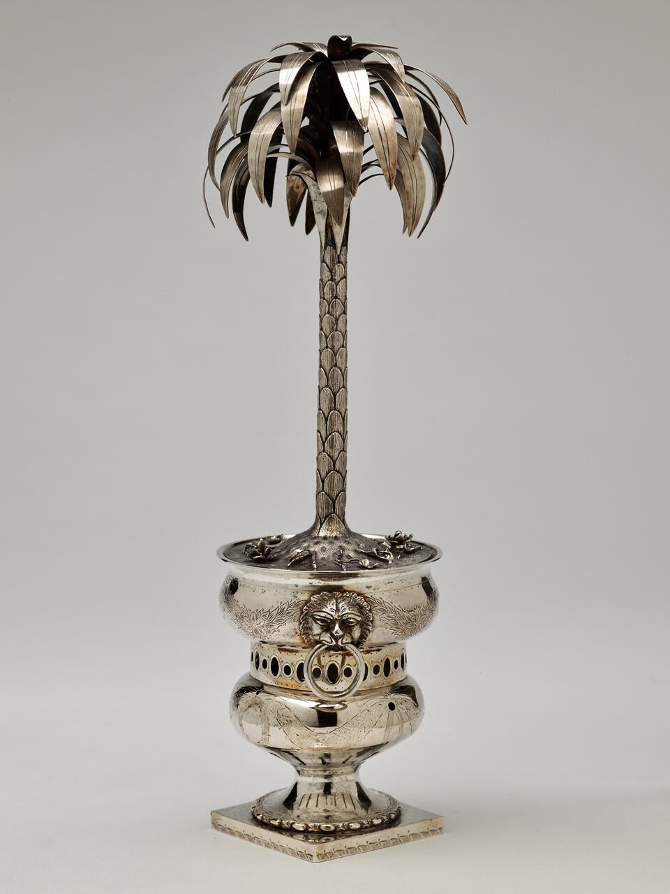 Silver sculpture in the shape of a palm tree, sitting inside an urn. 