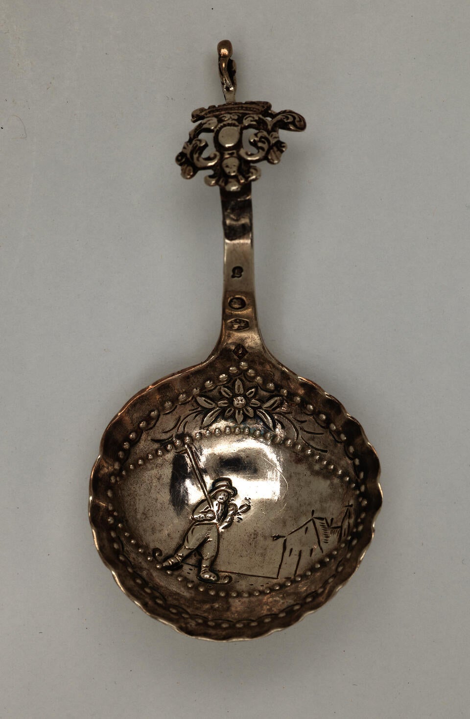 A silver caddy spoon with figurative and sculptural elements.