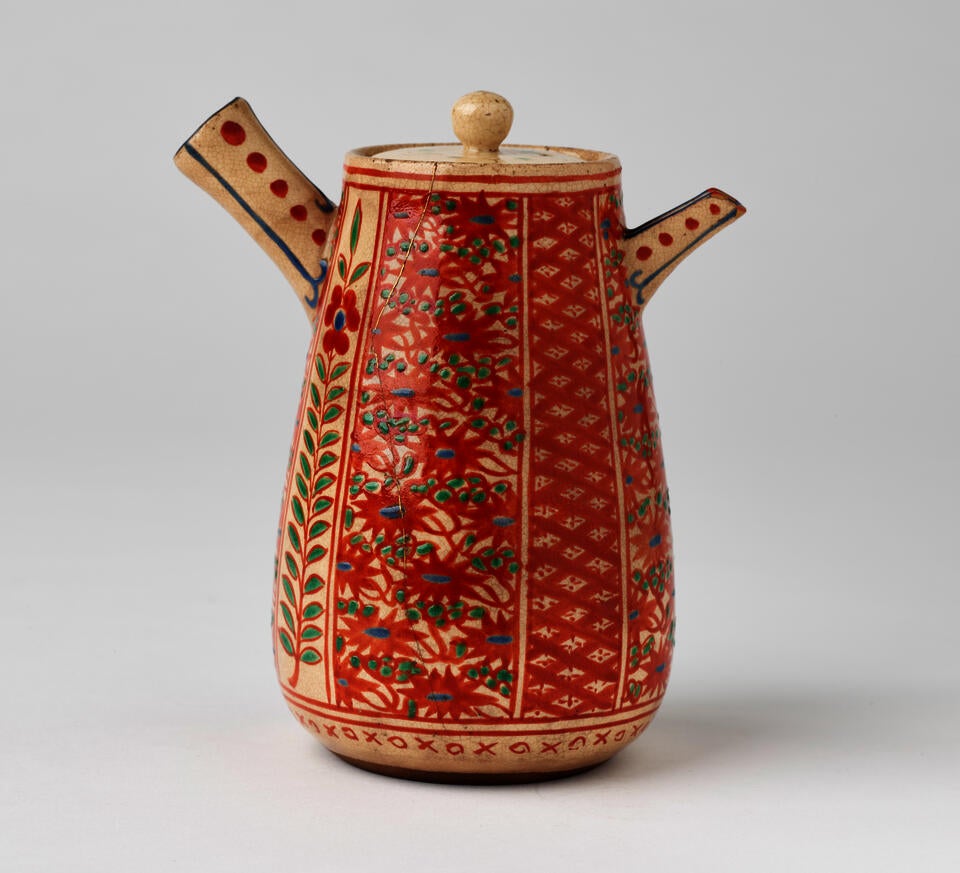 A stoneware teapot with enamel floral and abstract decorative motifs that are red, green, and blue. 