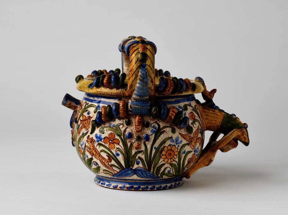 A yellow ceramic jug with floral decorations that are blue, green, and yellow. 