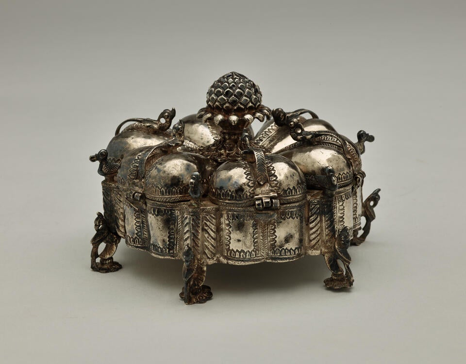 A dark silver spice box that is sculptural and has many different rounded compartments.