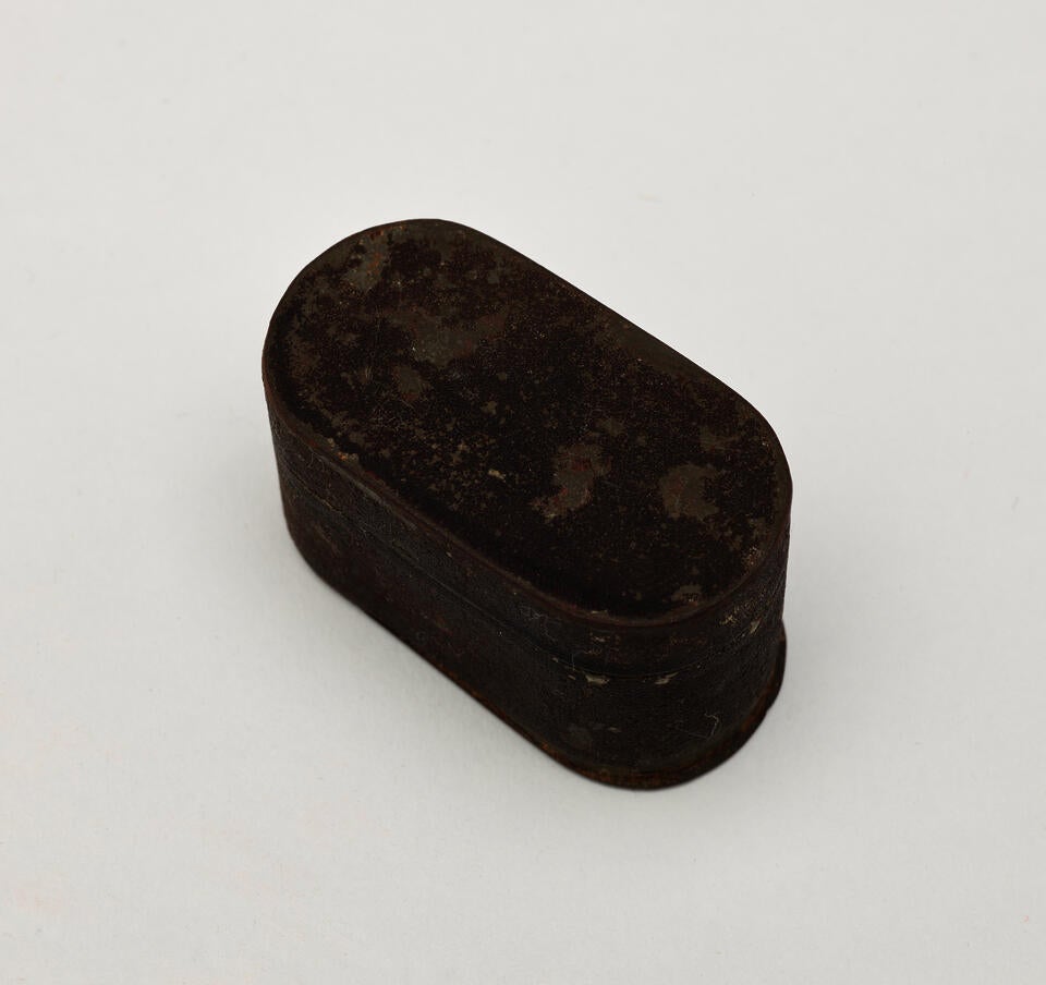 A tin and silver nutmeg grater, it has rounded corners and a shield on the lid. 