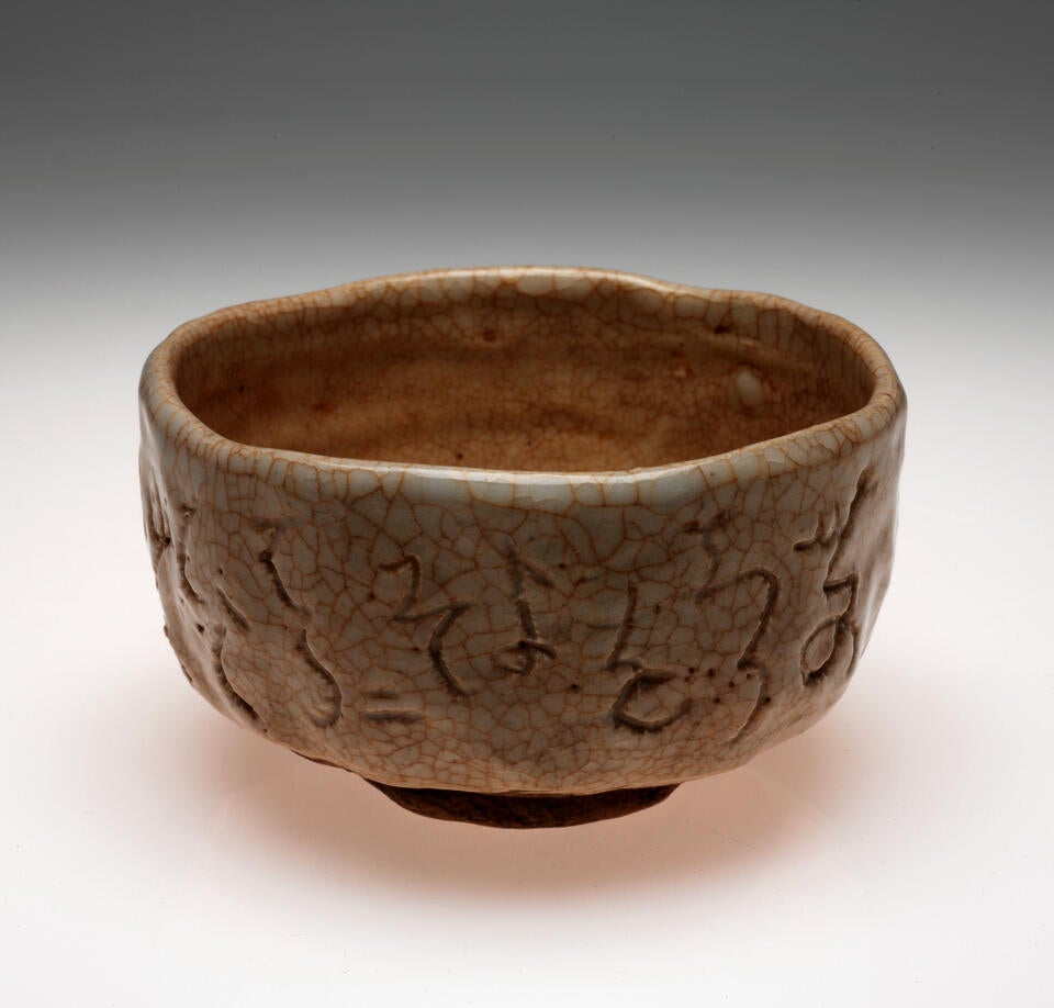 A bowl with undulating sides and rim. Cream and brown colored with a crackled surface and abstract designs scratched into the surface.