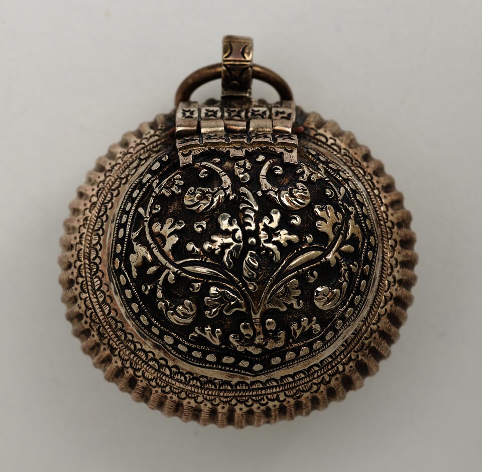 Rounded metal container with raised floral designs. A small circular metal ring attached to the top. 
