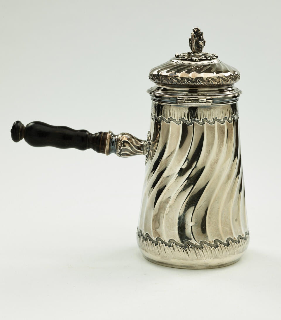 A silver chocolate pot with a decorative swirled body, lid, and fruit wood handle.
