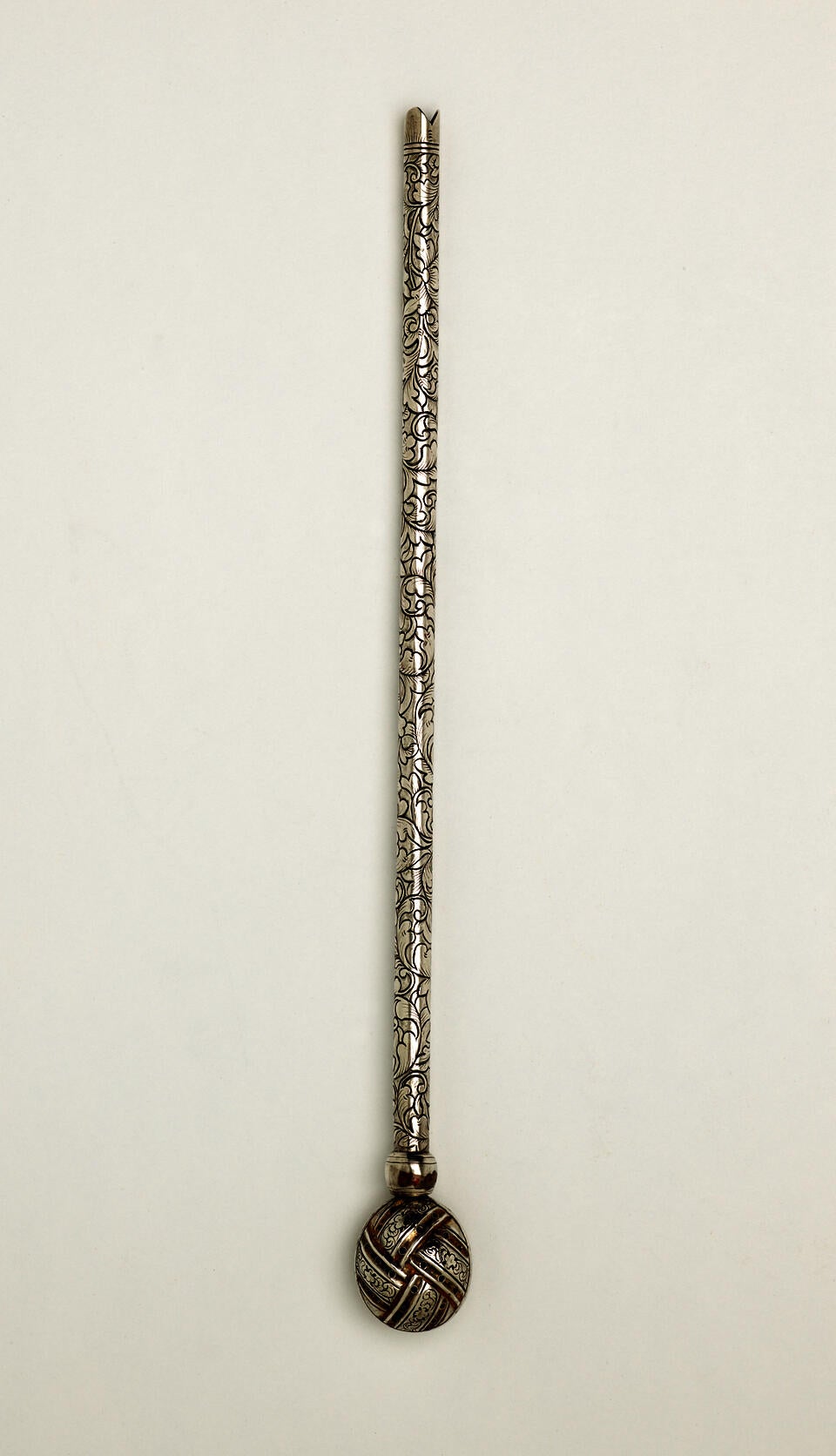 A long silver utensil used for tea with a decorative body and has one small bulbous end.