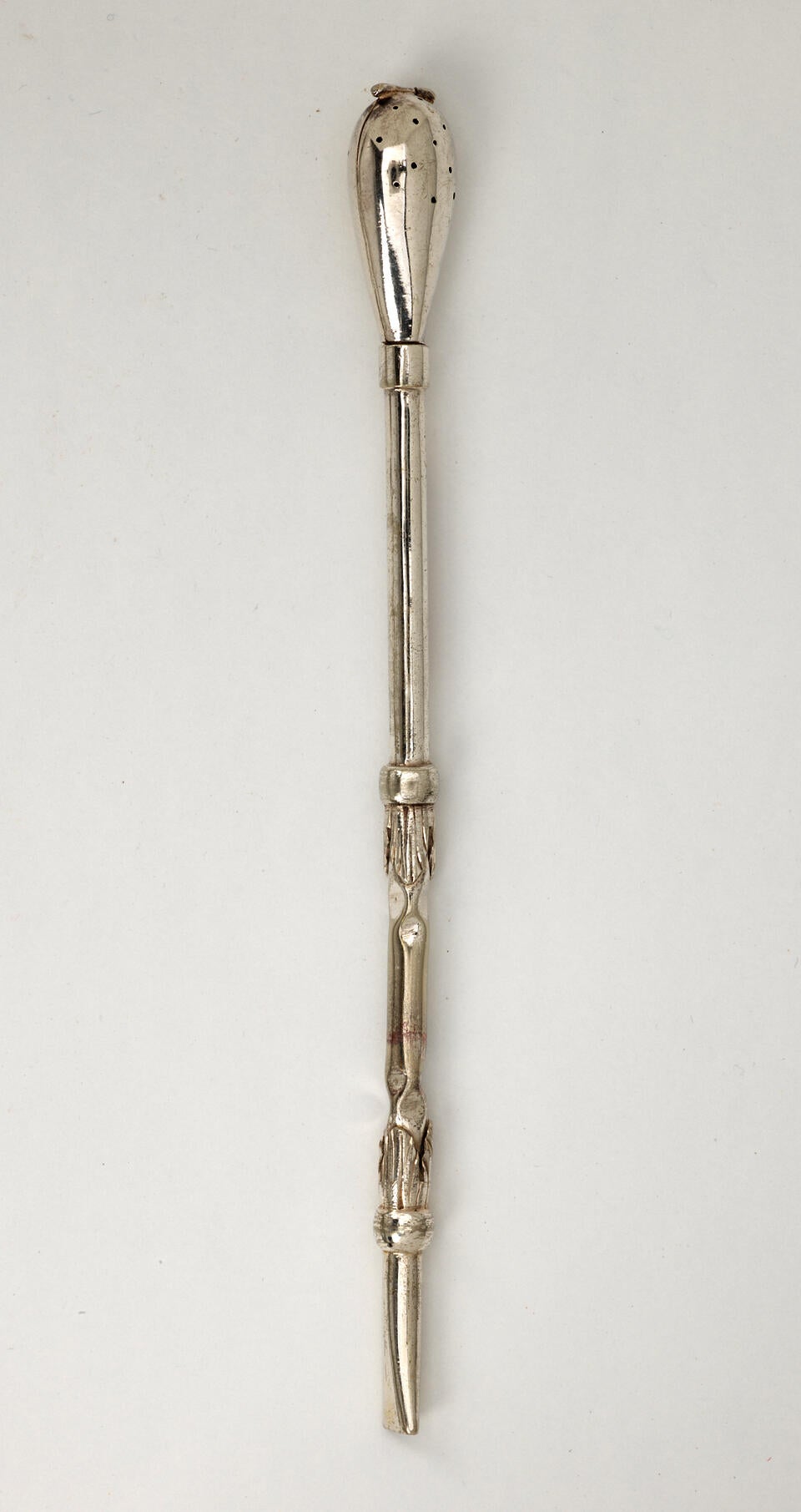A silver utensil used for steeping tea with a long skinny handle and bulbous end with small holes.