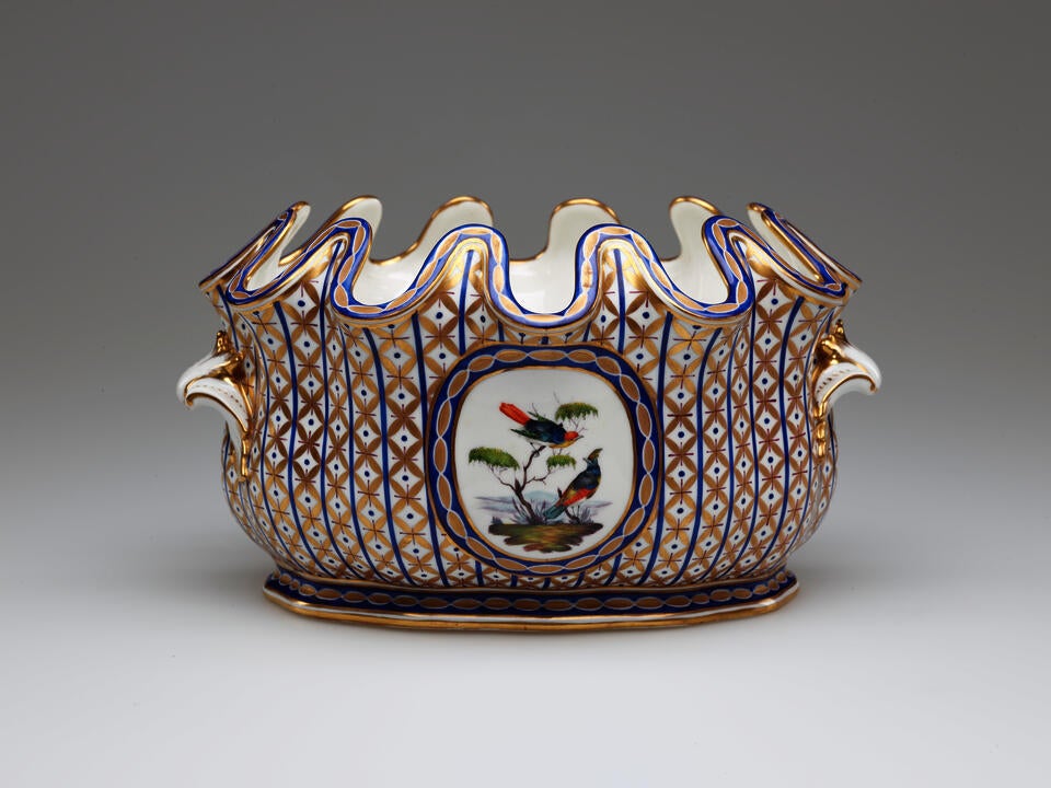 An open vessel with a deeply scalloped rim. A central decoration of two birds and a tree is surrounded by vertical bands of blue with gold diamond shapes. 