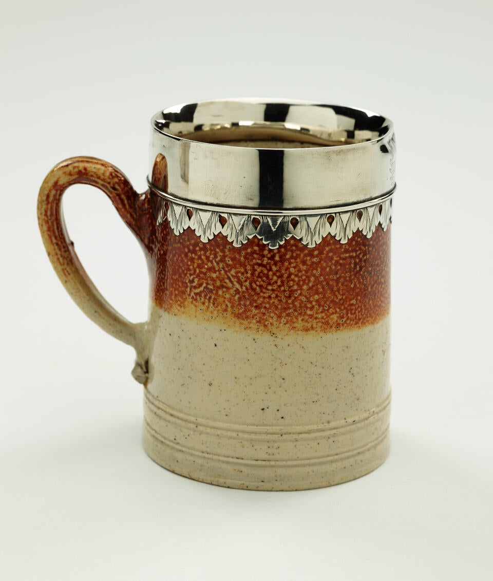 A salt glaze and silver mug with vertical decorative elements and one handle.