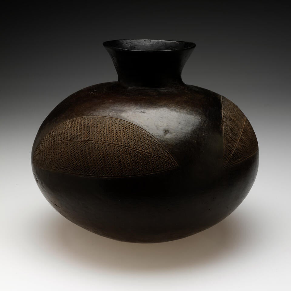A bulbous vessel with a rounded, flared neck. Two large, abstract leaf-shaped designs are scratched into the shiny surface. 