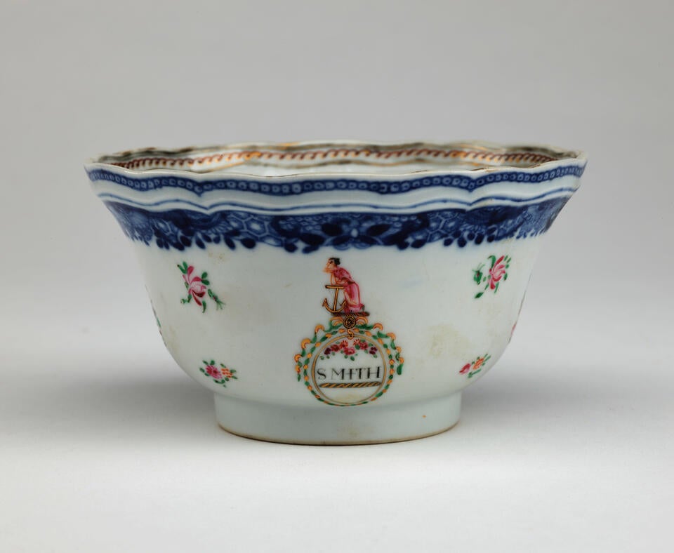 A porcelain sugar bowl with glided, blue, green, and pink decorations. The decorations are floral, as well as one figure, and a word saying “SMITH”.