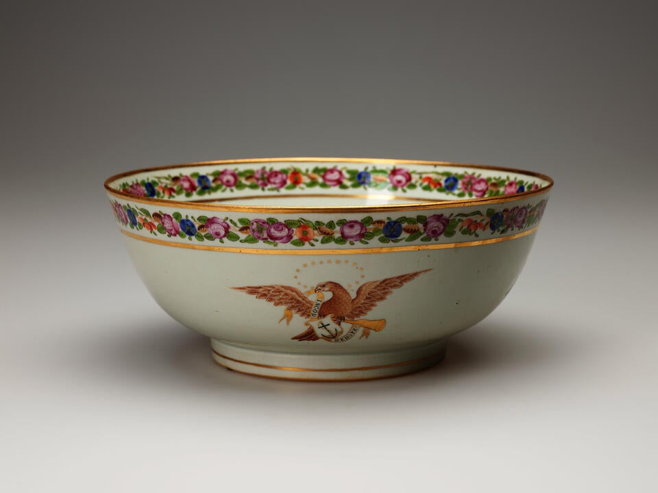 A white bowl with a flowered rim. Image of an eagle with an anchor in the center. 