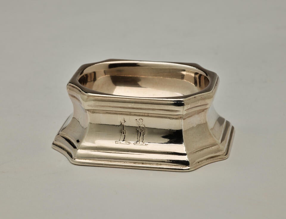 A silver salt container that is rounded on the inside and angular on the outside. 