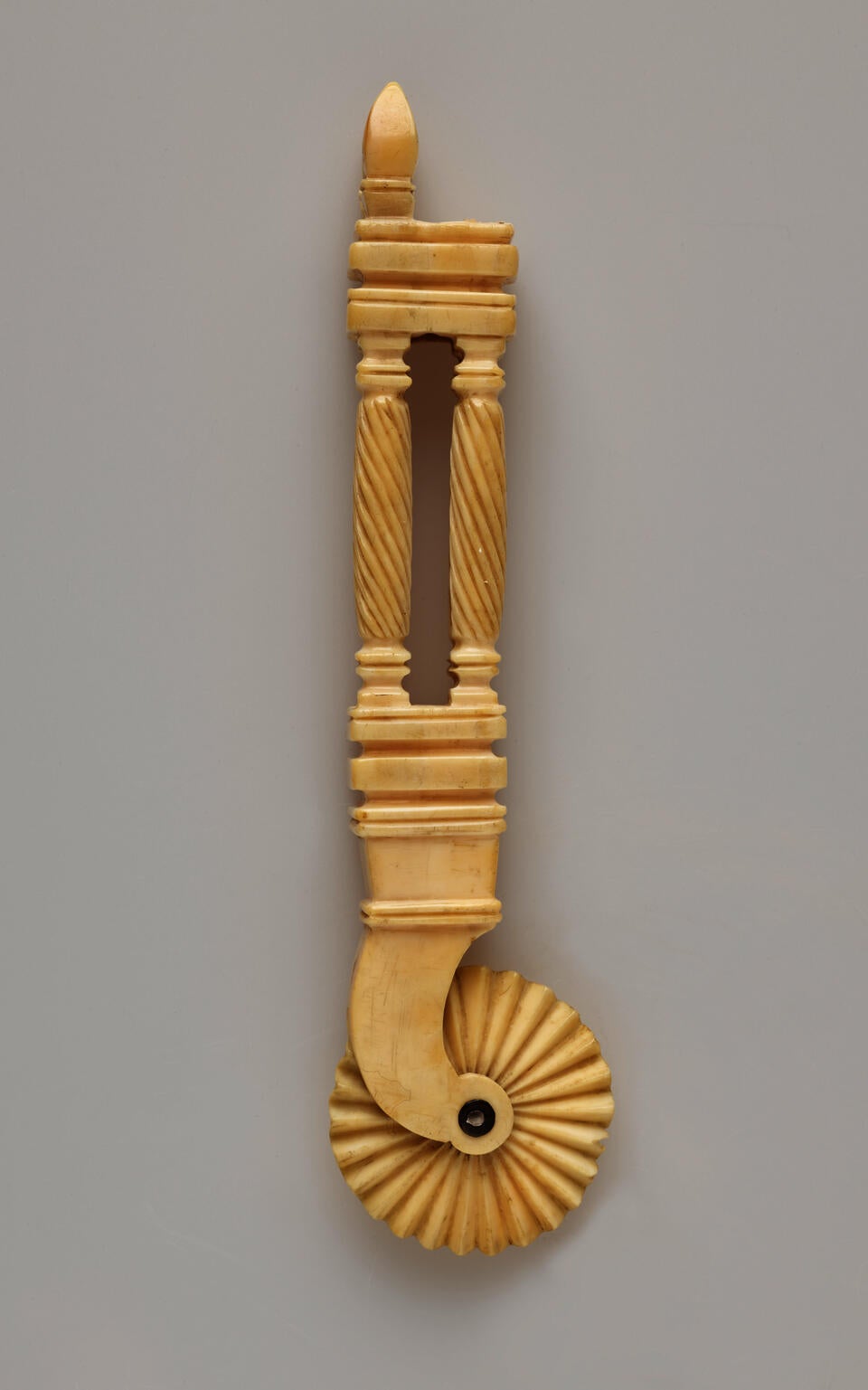 An ivory pie crimper with a decorative handle and a textured wheel. The handle has a cutout in the middle of it.