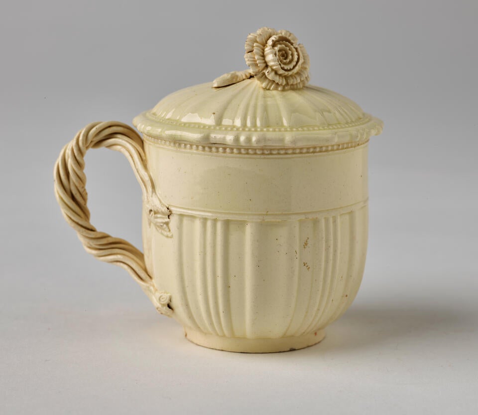 A white creamware custard cup, with a sculptural swirled handle, and lid with sculpted finial.