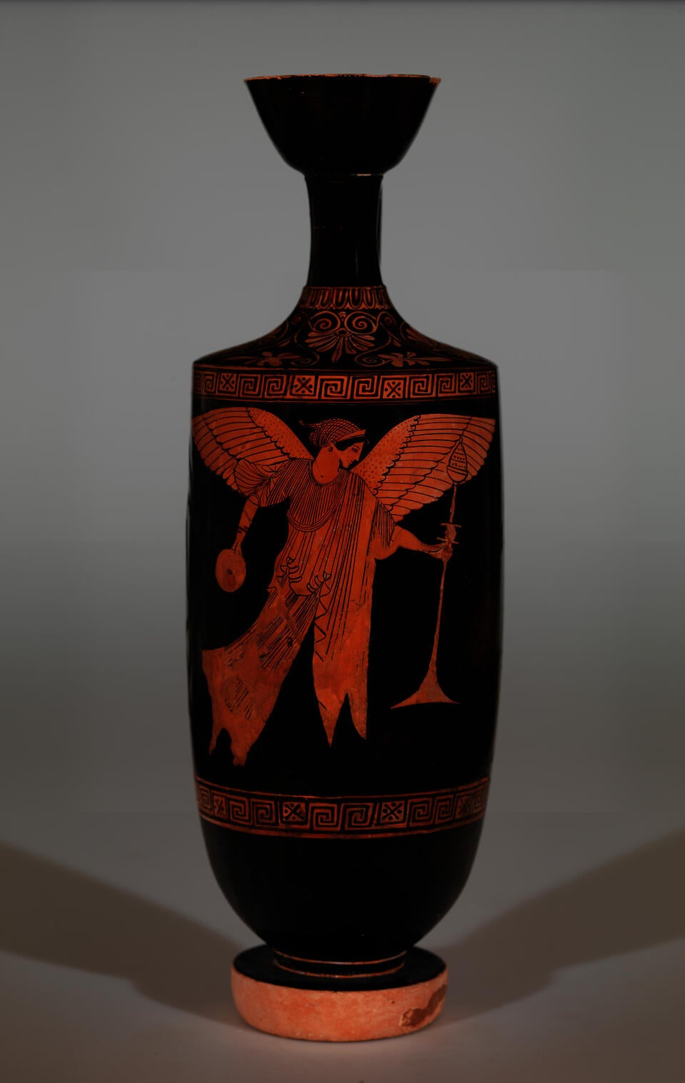 Vessel with an elongated, flared neck and unglazed foot. Decorated with a figure with wings holding a trumpet in one hand and a vessel in the other.