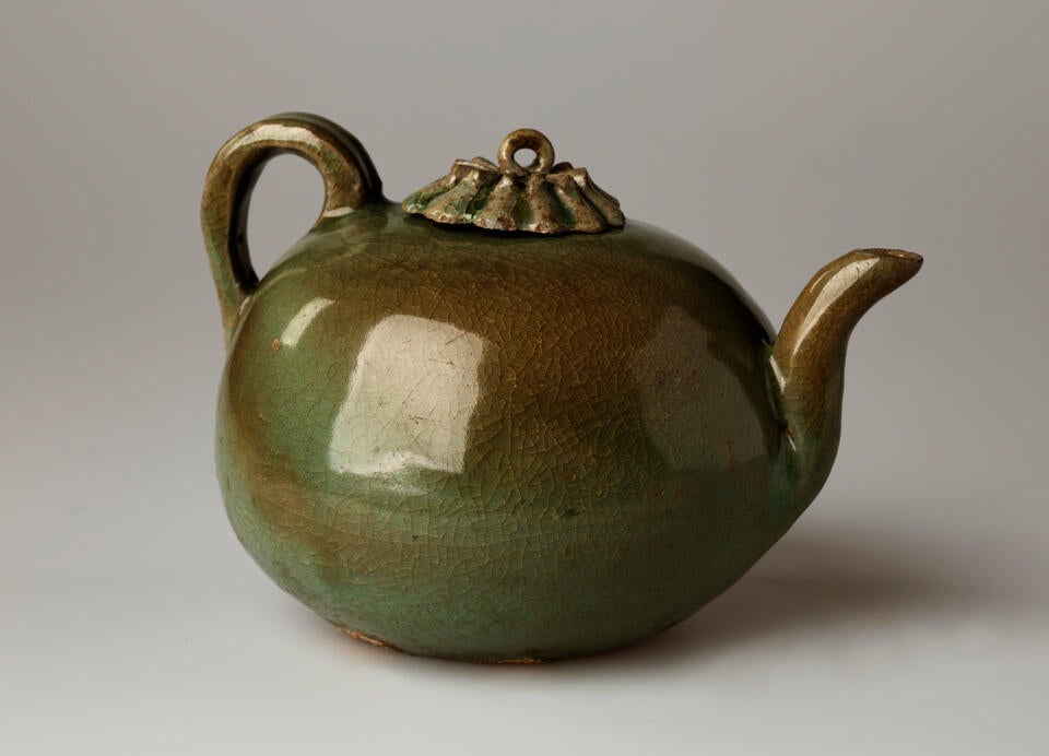 A rounded greenish brown water kettle with a handle, spout, and small decorative lid and a loop for a finial. 