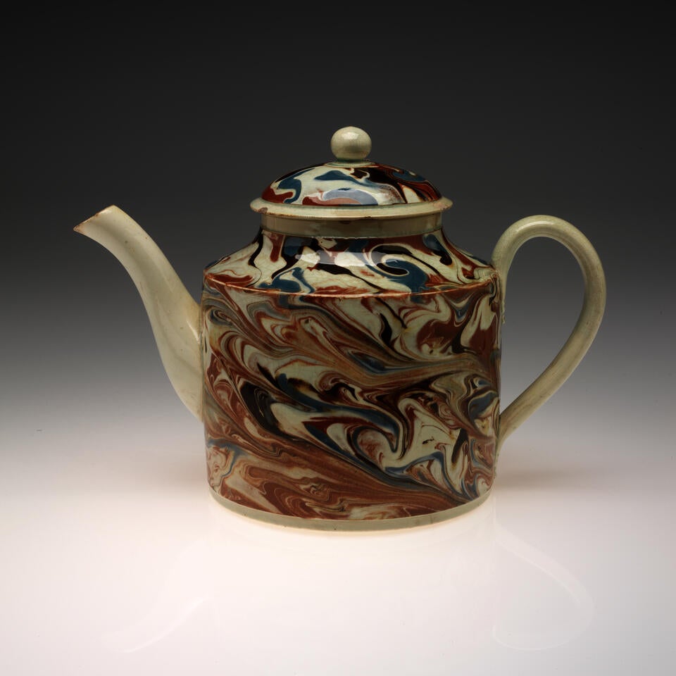 Teapot with a swirling, marbled design on the body and lid in brown, blue, black, and cream. Spout, handle, and rounded finial are solid cream colored. 
